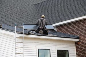 A roofer installing asphalt shingles on the roof of a detached single-family home in mild weather.