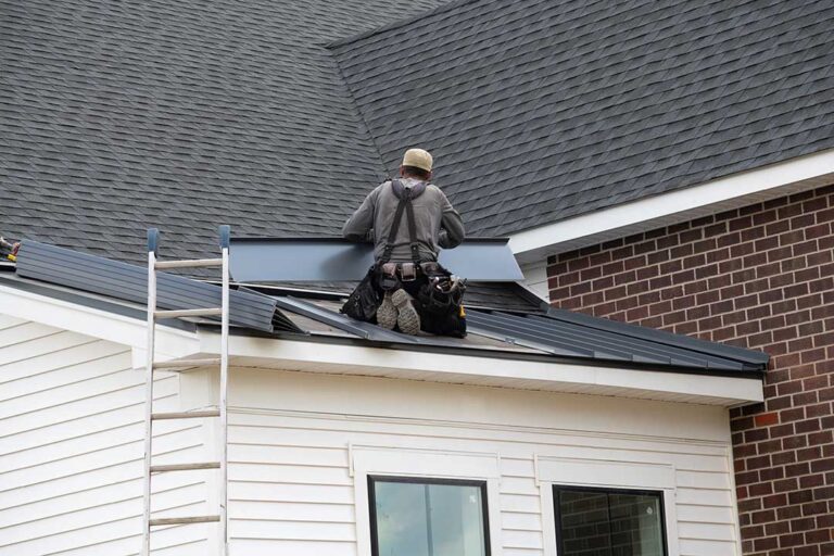 A roofer installing asphalt shingles on the roof of a detached single-family home in mild weather.