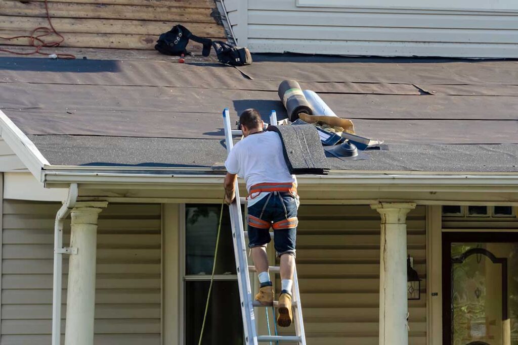 A person holding up a new shingle next to older, weathered shingles on a residential roof.