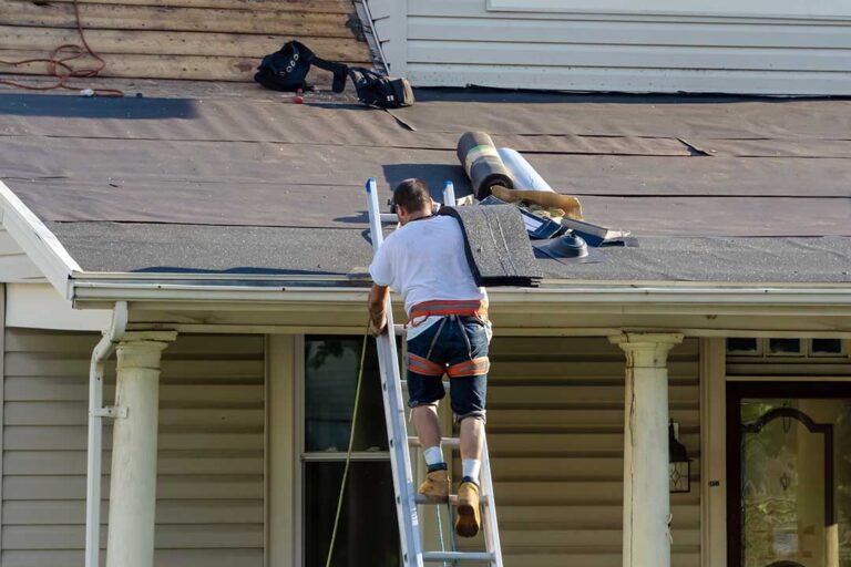 A person holding up a new shingle next to older, weathered shingles on a residential roof.